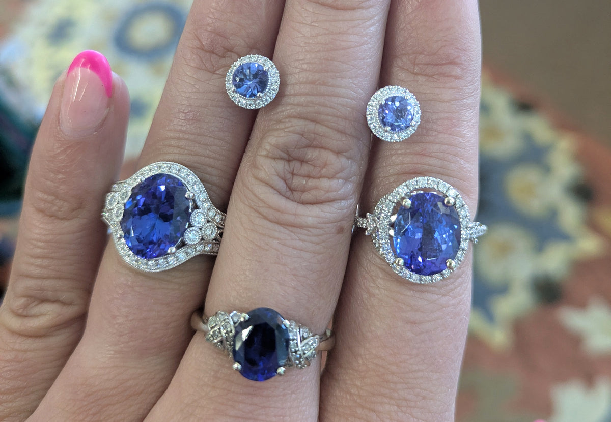 Three blue-stone rings and stud earrings displayed on a hand.